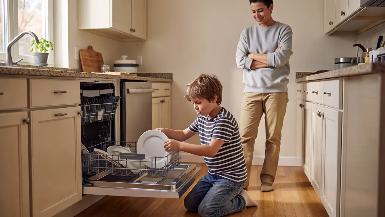 Young child loading dishwasher with parental supervision